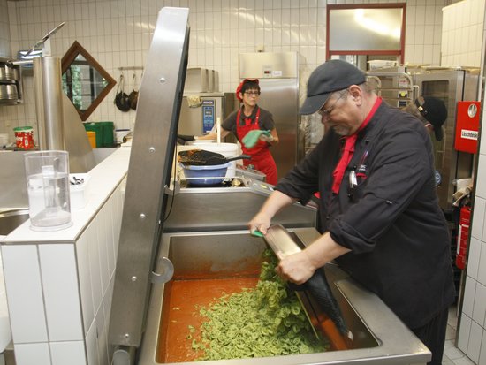 ein Koch schüttet Nudeln in rote Sauce